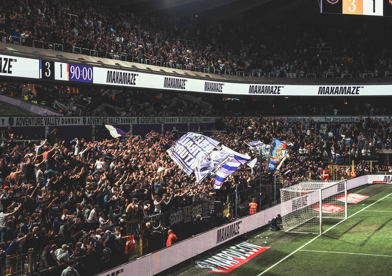 A packed stand behind a stadium perimeter LED run carrying sponsor banners at full time